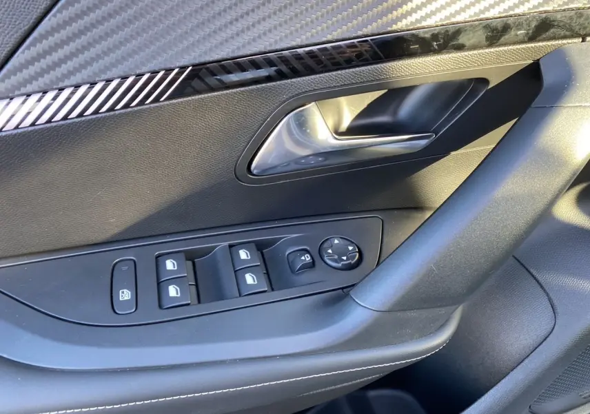 Gros plan sur la porte côté gauche du Peugeot 2008 gris Artense, montrant les commandes des vitres et la poignée intérieure chromée.