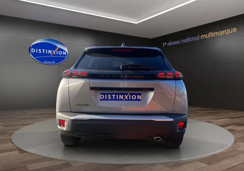 Vue arrière d'un Peugeot 2008 gris Artense 2024 avec feux LED et sortie d'échappement visible sur fond showroom.