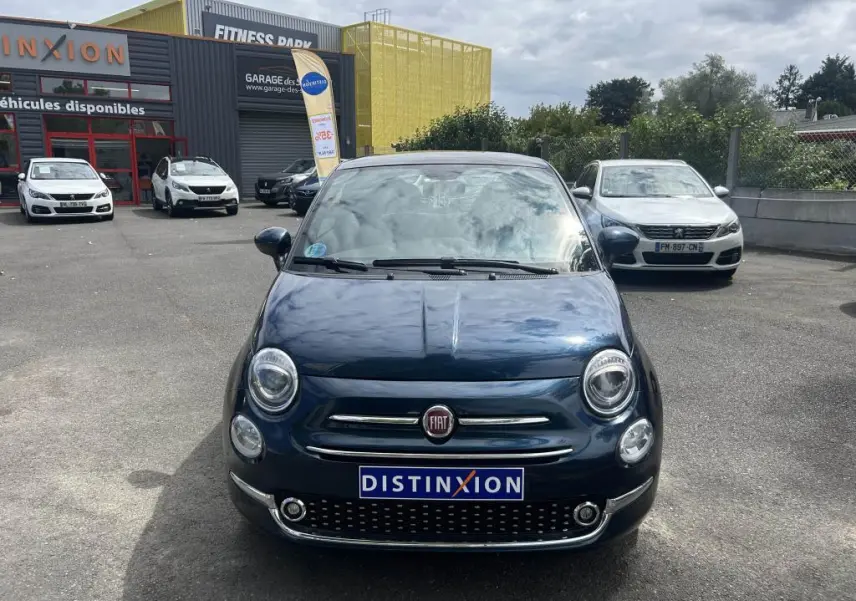 Vue de face d'une Fiat 500 2024 bleu avec toit vitré panoramique et jantes alliage 16'' Spider sur parking.