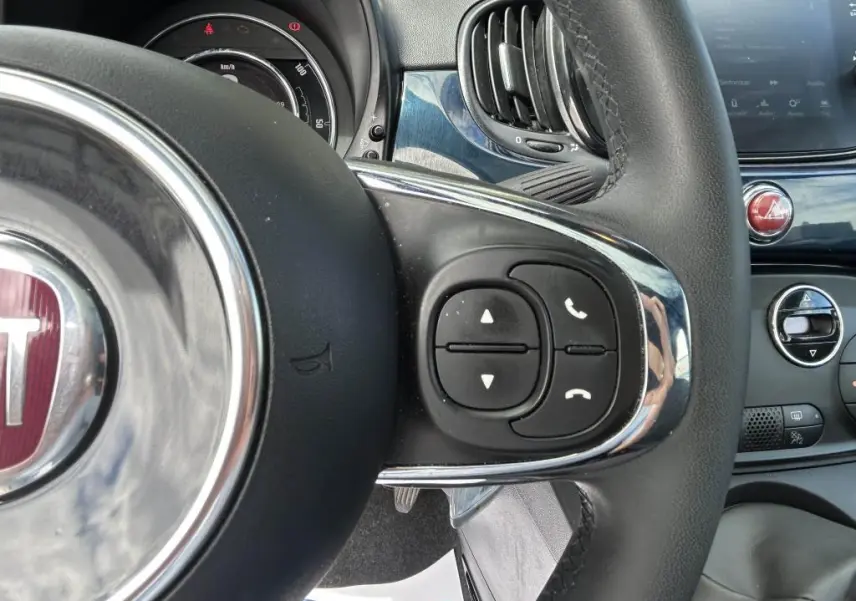 Gros plan sur les commandes au volant du FIAT 500 bleu 2024, avec tableau de bord et ventilation visibles en arrière-plan.