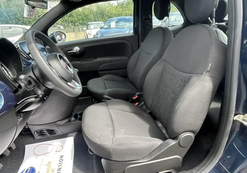 Intérieur de la FIAT 500 2024 bleu, vue côté gauche montrant les sièges avant en tissu noir et le volant multifonction.