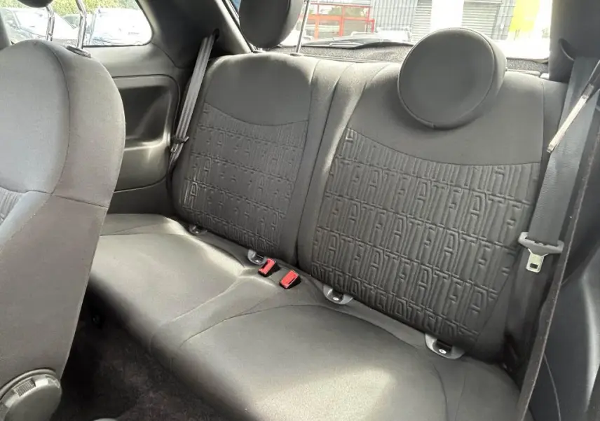 Vue intérieure arrière du siège noir de la Fiat 500 2024 avec motifs FIAT embossés et ceintures de sécurité visibles.