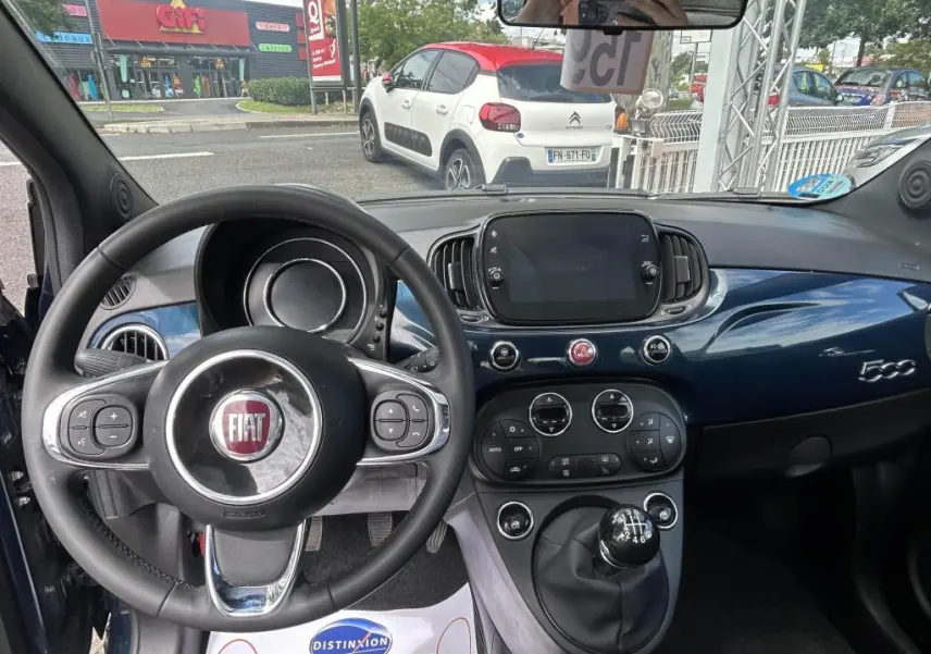 Vue intérieure avant du tableau de bord bleu et volant multifonction du FIAT 500 2024 avec boîte manuelle et écran tactile central.