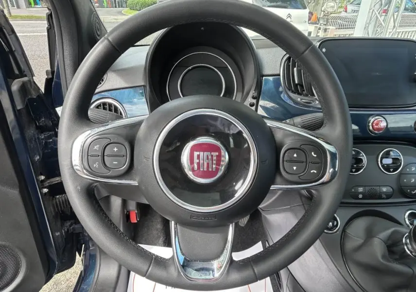 Vue intérieure centrée sur le volant de la Fiat 500 bleu 2024 avec commandes au volant et tableau de bord assorti.