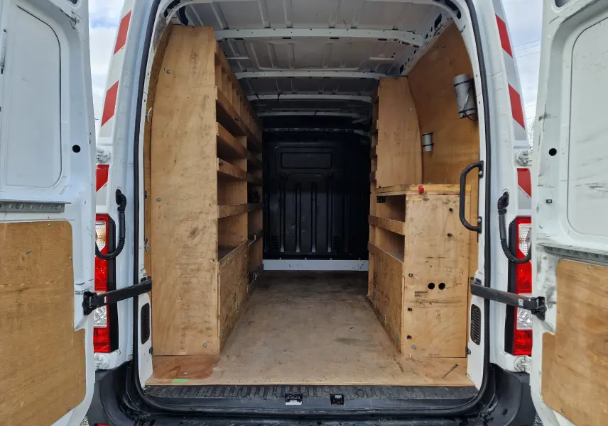 Vue arrière ouverte du Renault Master blanc 2020, montrant l'aménagement intérieur en bois avec étagères et rangements intégrés.
