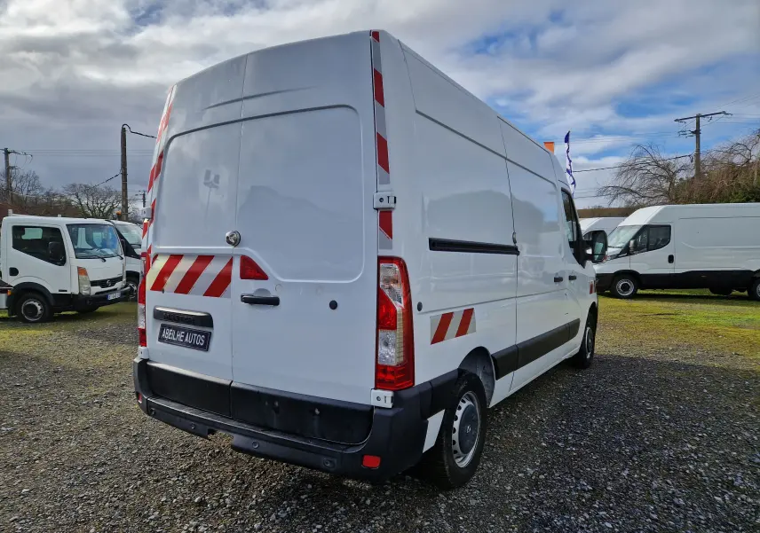 Vue 3/4 arrière droite d’un utilitaire Renault Master blanc avec bandes réfléchissantes rouges sur fond blanc.