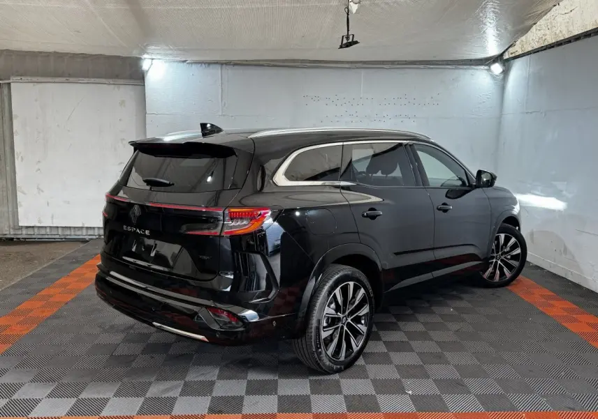 Renault Espace noir en 3/4 arrière droit, avec rails de toit chromés et feux arrière LED allumés dans un garage.