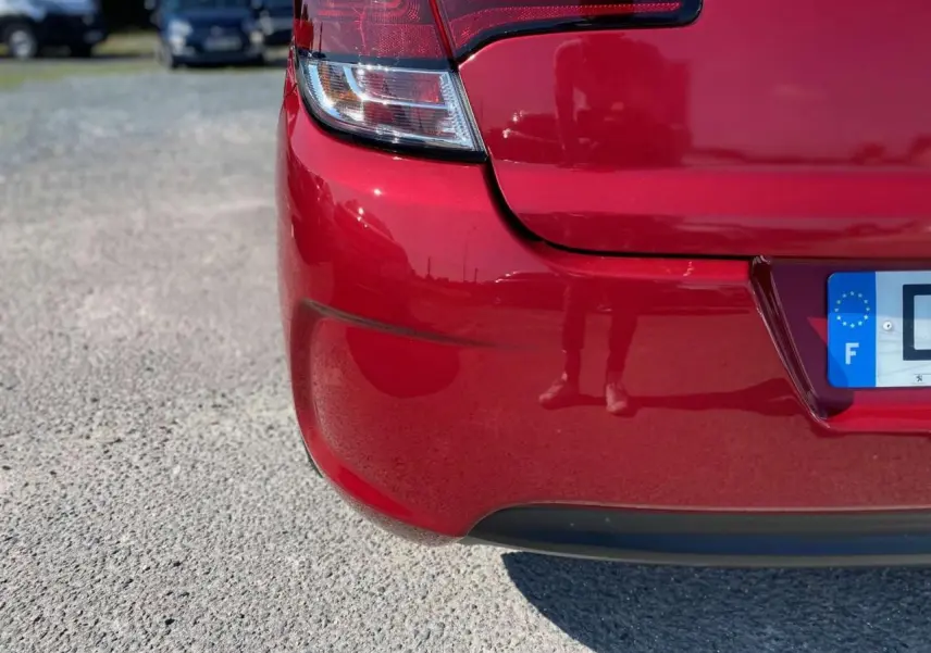 Gros plan sur le coin arrière gauche rouge métallisé d'une Citroën C4 Millenium avec feu arrière et plaque d'immatriculation française visible.