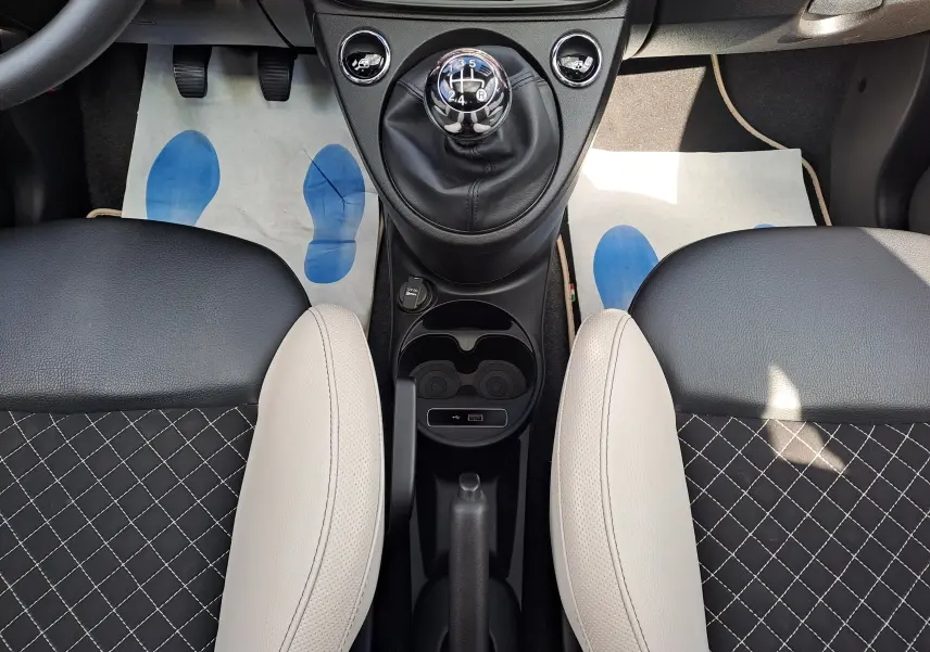 Vue plongeante sur la console centrale et les sièges bicolores noir et beige de la Fiat 500 2020 avec levier de vitesse manuel.