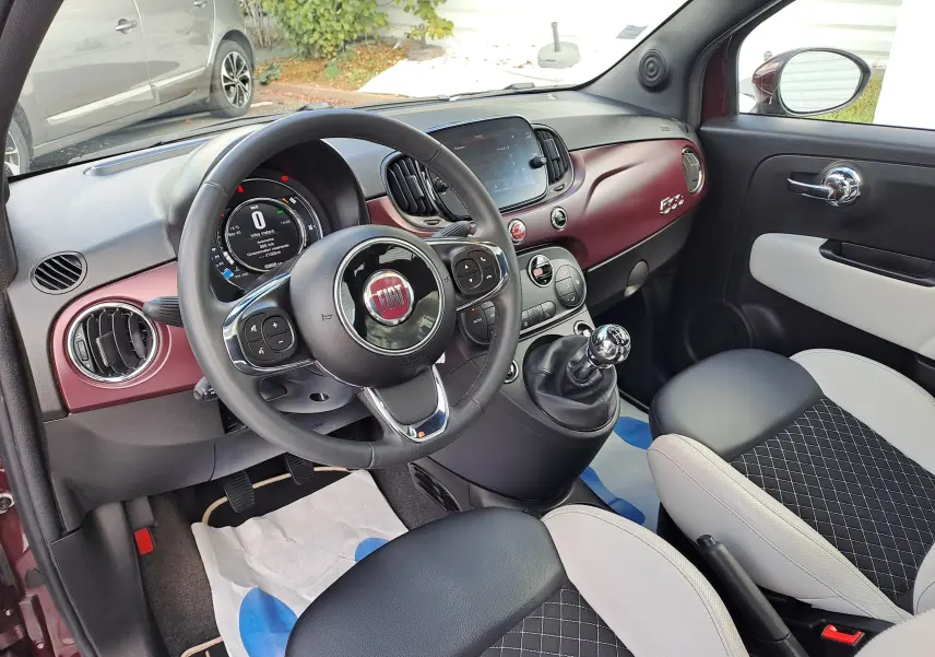 Vue intérieure côté conducteur de la Fiat 500 2020 avec tableau de bord bordeaux Opera et sièges bi-color noir et beige.