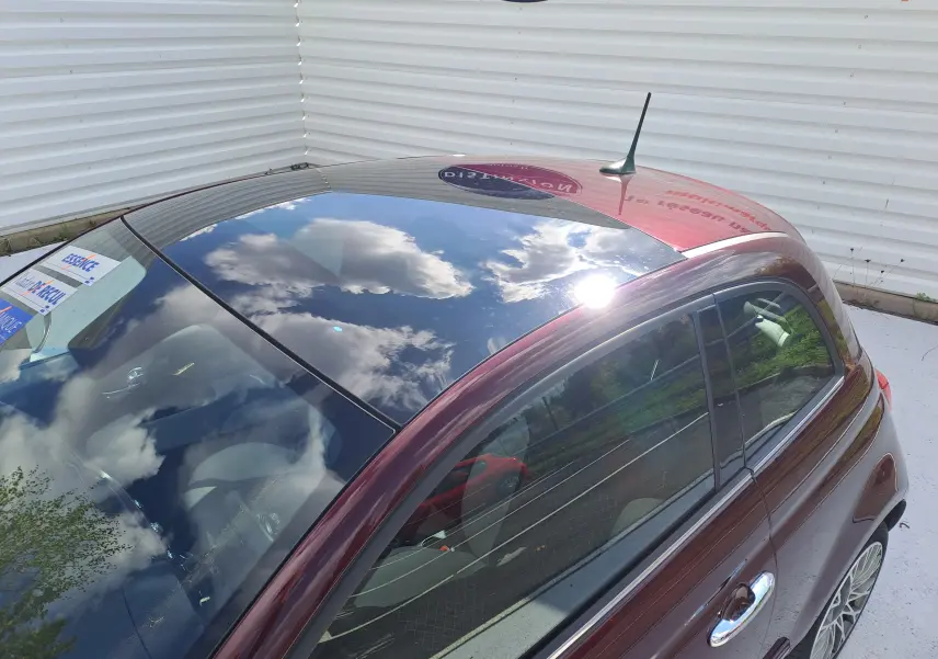 Vue plongeante sur le côté gauche d'une Fiat 500 Opera Bordeaux Métal 2020 avec toit vitré brillant et intérieur clair.