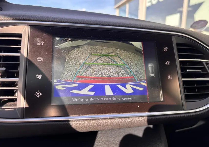 Écran tactile intérieur affichant la caméra de recul d'une Peugeot 308 GT Line rouge foncé, avec lignes de guidage colorées.