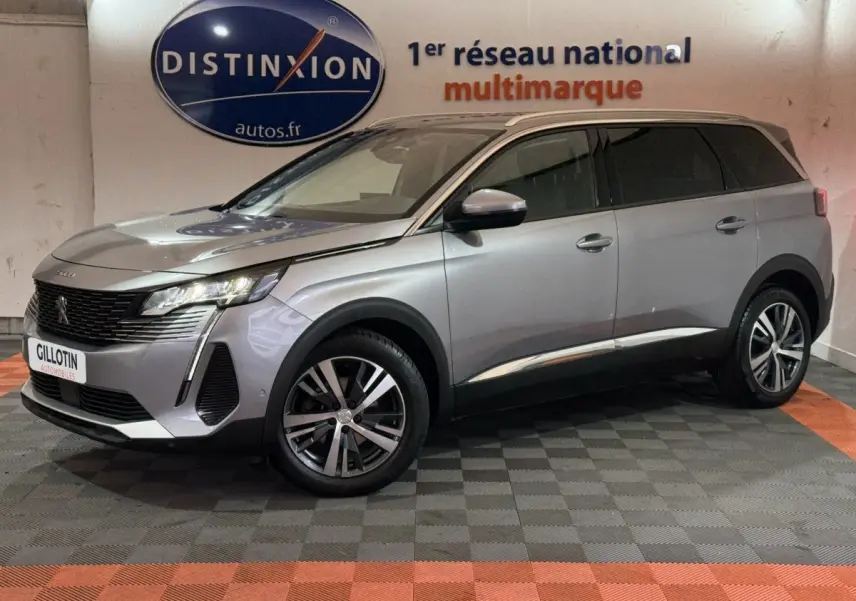 Peugeot 5008 gris clair en vue 3/4 avant droit, avec jantes alliage et phares LED allumés en intérieur showroom.