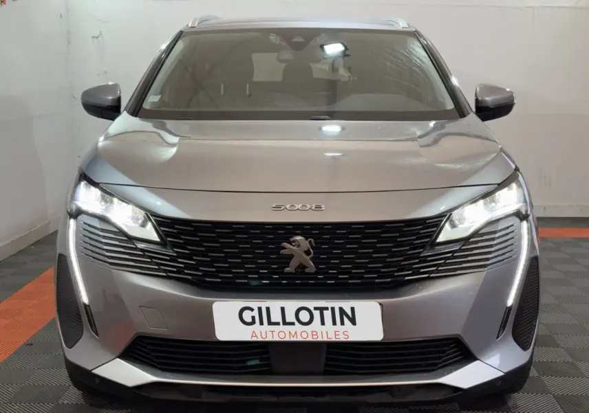 Vue frontale d’un Peugeot 5008 gris clair avec phares LED allumés et calandre noire distinctive.