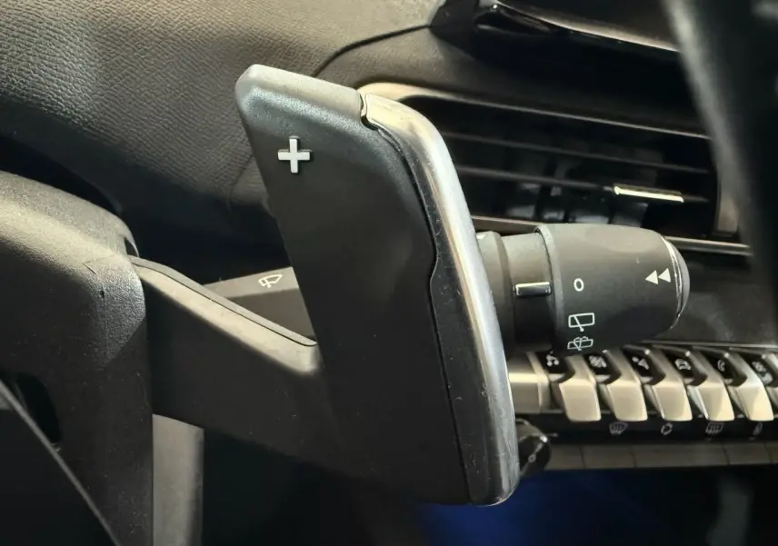 Gros plan sur la palette de changement de vitesse + côté droit du volant noir dans l’habitacle d’un Peugeot 5008 gris clair.