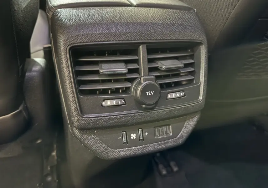 Gros plan sur la console arrière noire du Peugeot 5008 2021 avec ventilation, prise 12V et commandes climatisation.