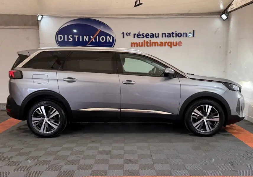 Profil droit d'un Peugeot 5008 gris clair 2021, SUV familial avec jantes alliage et vitres teintées, en intérieur showroom.