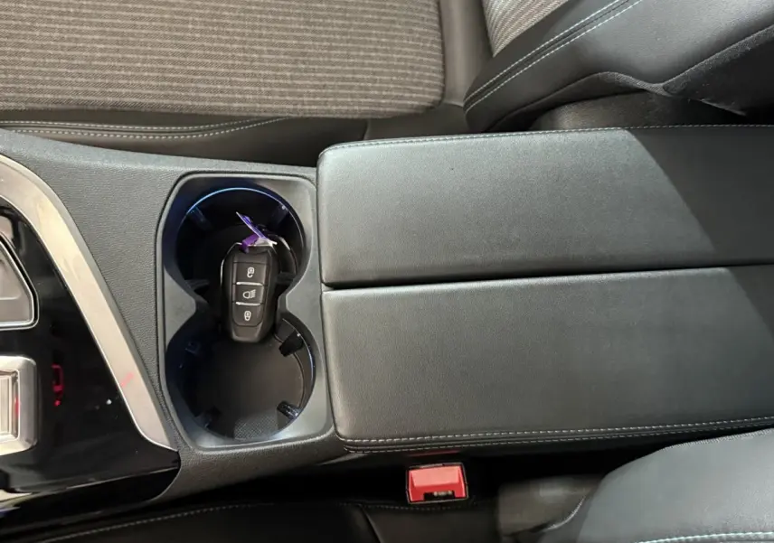 Vue rapprochée de la console centrale noire avec porte-gobelets et clé de voiture Peugeot 5008 posée dedans.