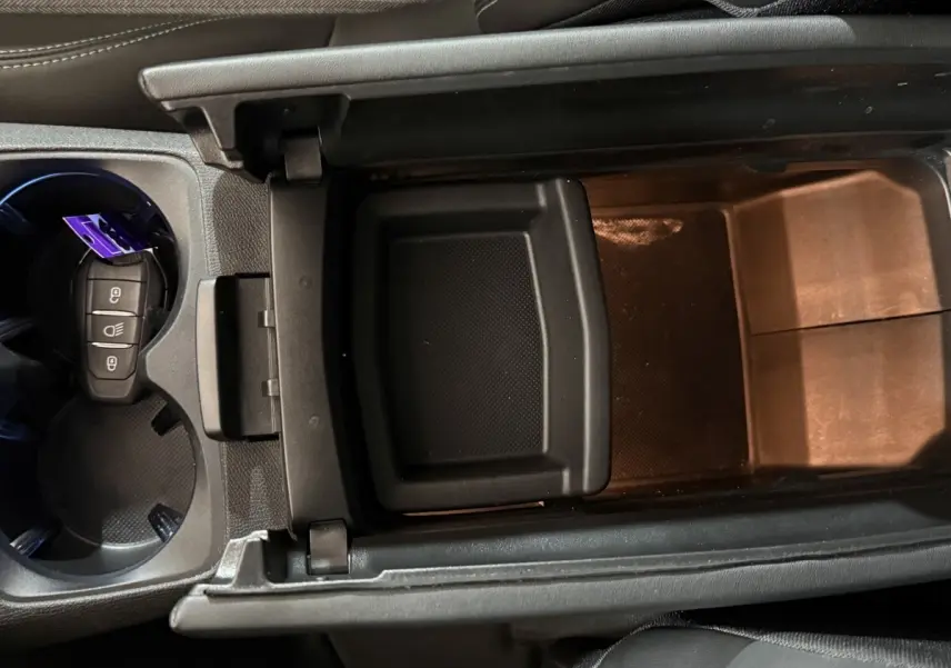 Vue rapprochée de la console centrale ouverte du Peugeot 5008 gris clair, avec porte-clés dans porte-gobelets.