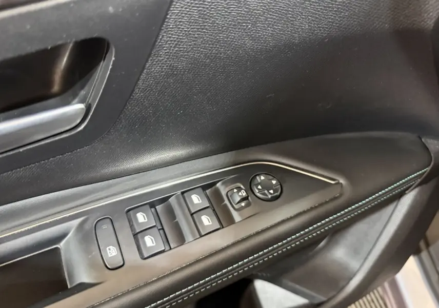 Gros plan sur la commande des vitres électriques côté gauche, avec surpiqûres bleues sur le panneau de porte noir.