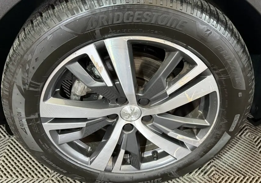 Gros plan sur la roue avant droite du Peugeot 5008 gris clair, jante alliage à design moderne avec logo lion central.