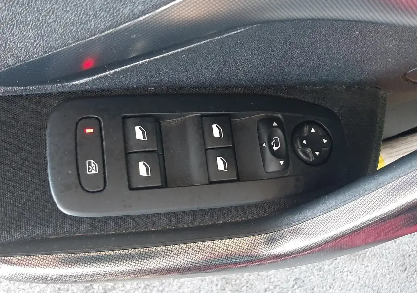 Gros plan sur les commandes électriques des vitres côté gauche d'une Peugeot 2008 rouge de 2016, version Allure.