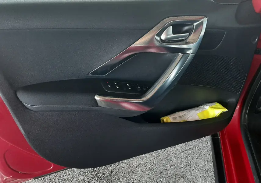 Porte côté gauche ouverte d'un Peugeot 2008 rouge, avec commandes de vitres et poignée argentée visible.