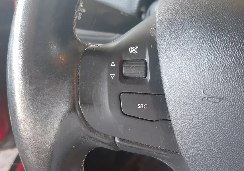 Gros plan sur les commandes audio au volant noir du Peugeot 2008 rouge 2016, bouton SRC et molette de volume.
