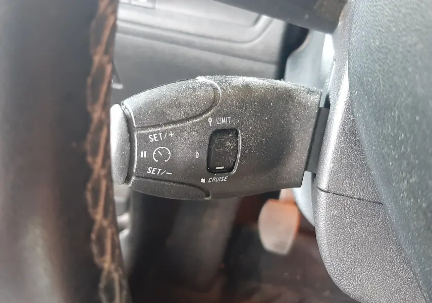 Gros plan sur la commande de régulateur de vitesse à gauche du volant d'un Peugeot 2008 rouge de 2016.