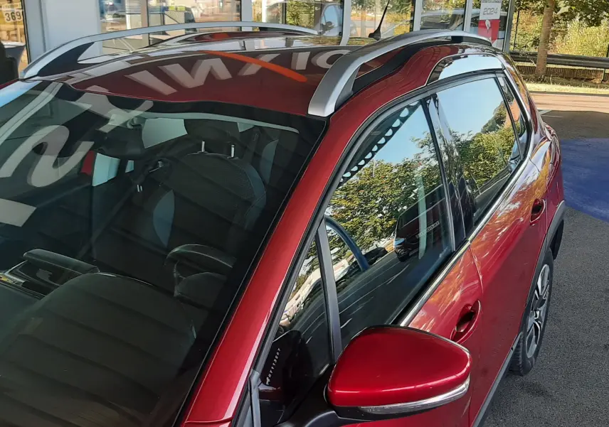 Vue de côté droit avant du Peugeot 2008 rouge avec barres de toit argentées et rétroviseur assorti.