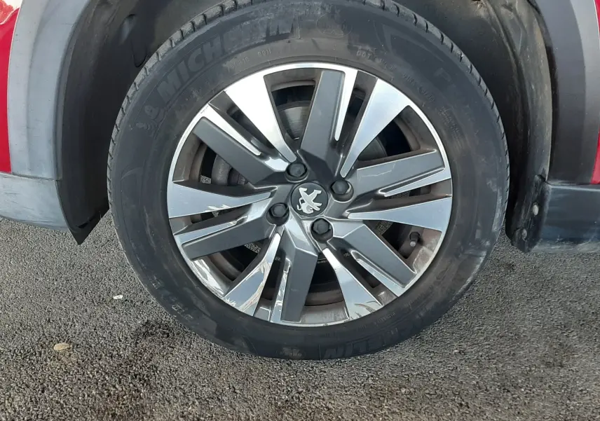 Gros plan sur la roue avant gauche d'une Peugeot 2008 rouge, jante alliage à motif moderne et pneu Michelin visible.