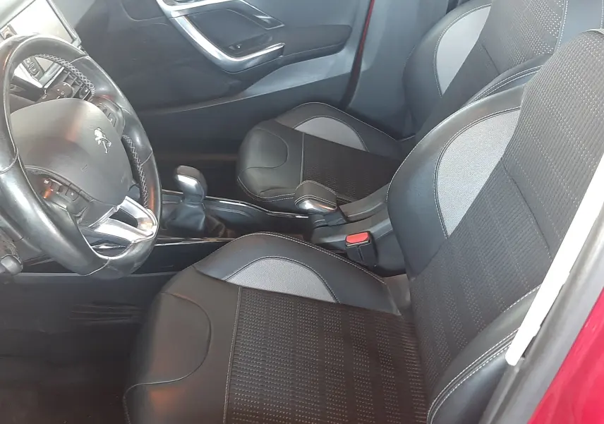 Intérieur avant droit d'une Peugeot 2008 rouge de 2016, sièges noirs en tissu et cuir avec volant multifonction visible.