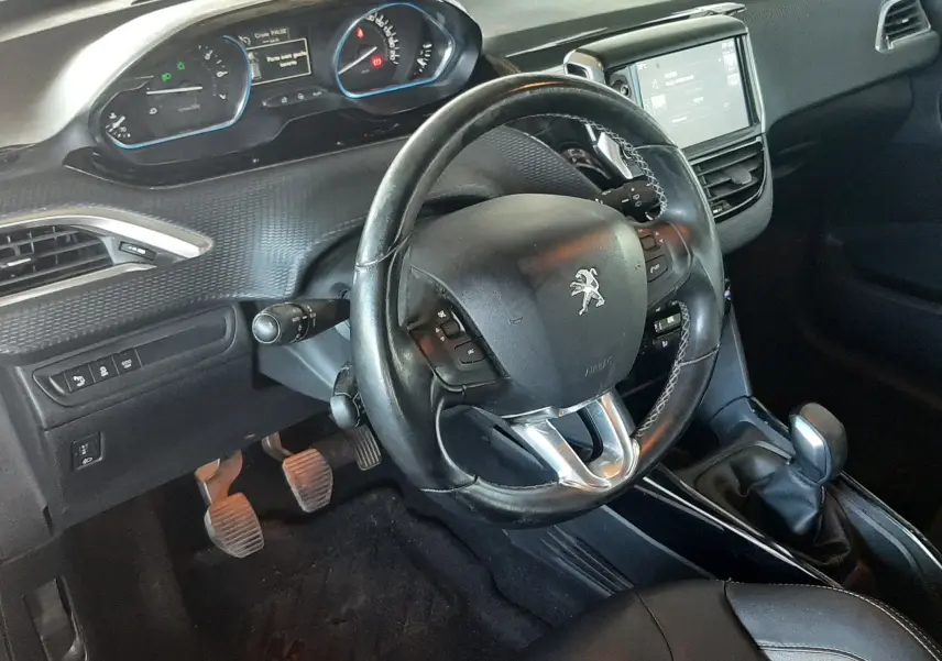 Vue intérieure côté conducteur du Peugeot 2008 rouge de 2016, volant multifonction et tableau de bord numérique visibles.