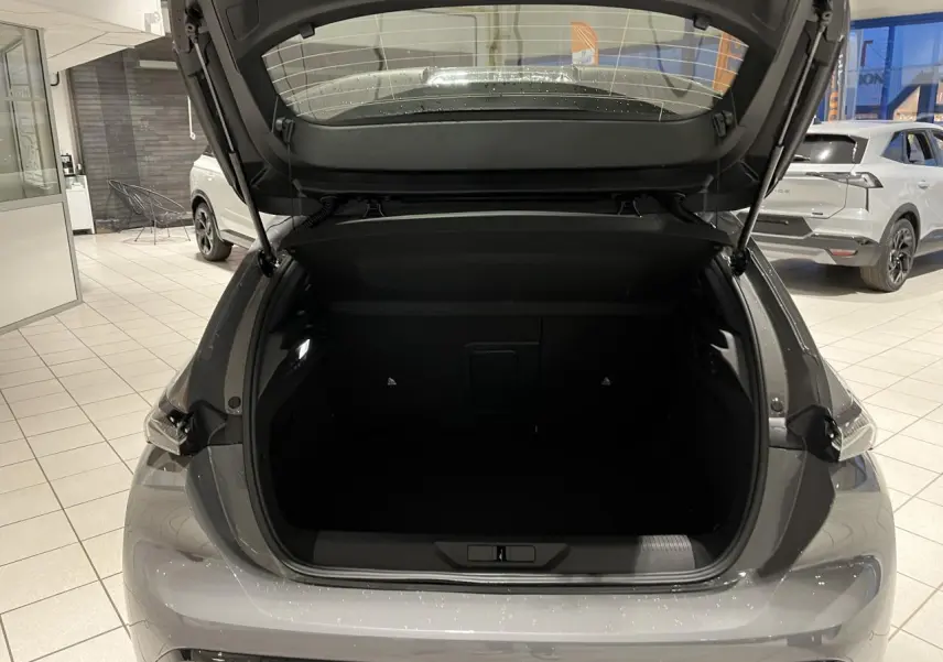 Coffre ouvert vu de l'arrière d'une Peugeot 308 gris selenium dans un showroom lumineux.