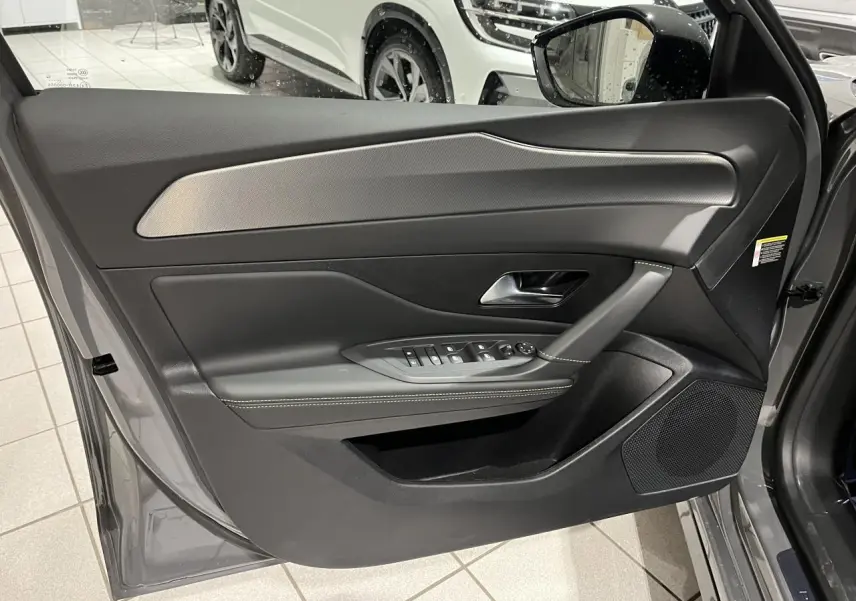 Porte avant gauche ouverte d'une Peugeot 308 gris selenium, avec garniture noire et surpiqûres claires.