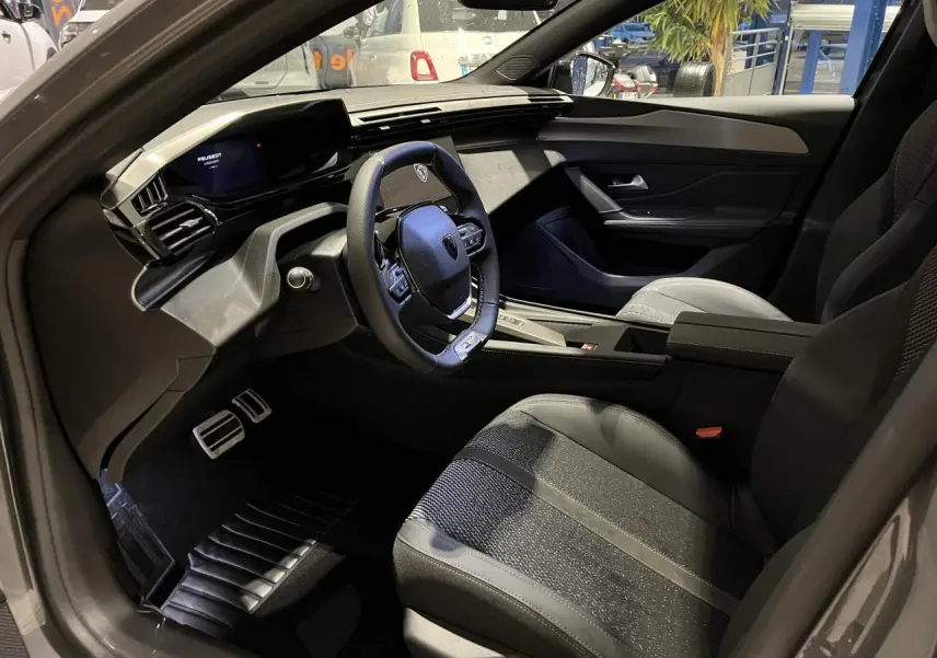 Intérieur de la Peugeot 308 GT 2024 vu côté conducteur, avec volant cuir et sellerie tissu/TEP gris.