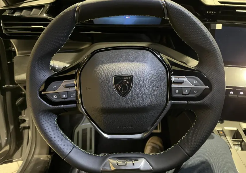 Volant cuir noir avec surpiqûres vertes et logo GT au centre d'une Peugeot 308 GT 2024, vue de face rapprochée.