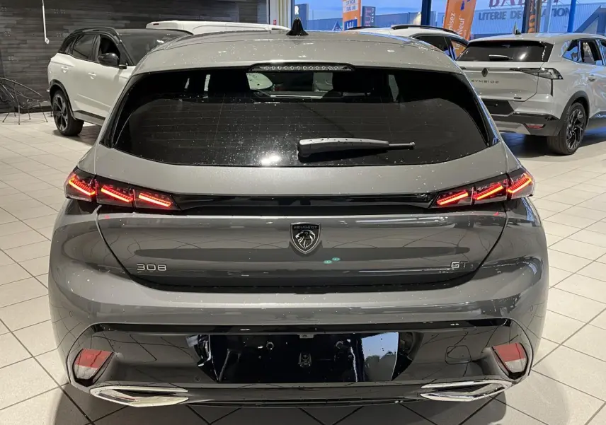 Vue arrière d'une Peugeot 308 GT gris sélénium avec feux arrière LED griffés et jantes alliage visibles en intérieur showroom.