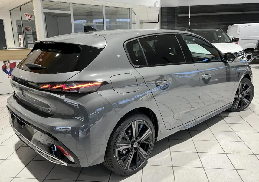 Peugeot 308 GT gris sélénium vue 3/4 arrière droit en intérieur avec jantes alliage noires et feux LED distinctifs.