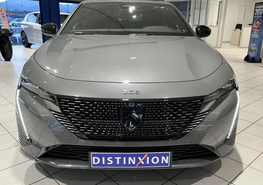 Vue de face d'une Peugeot 308 gris sélénium avec calandre noire brillante et feux LED dynamiques en showroom.