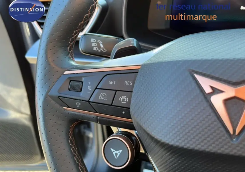 Gros plan sur le volant en cuir perforé noir avec surpiqûres cuivrées et logo CUPRA en relief cuivré.