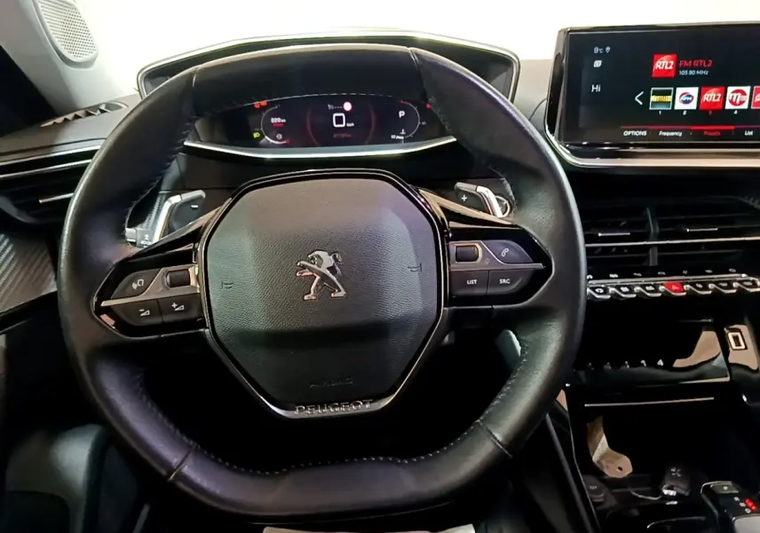 Vue rapprochée du volant cuir multifonctions noir et du tableau de bord numérique du Peugeot 2008 blanc 2021.