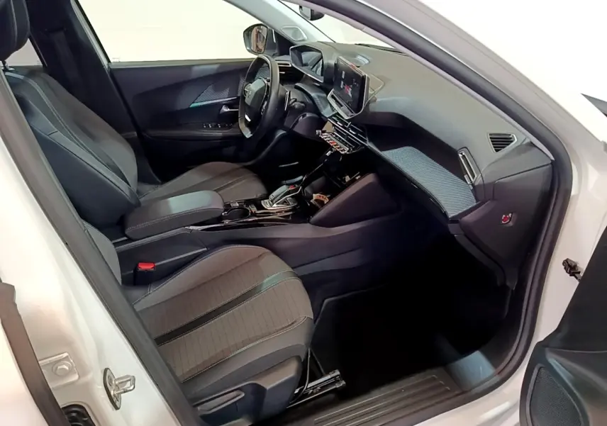 Intérieur côté conducteur du Peugeot 2008 blanc, montrant sièges tissu, volant cuir multifonctions et tableau de bord moderne.