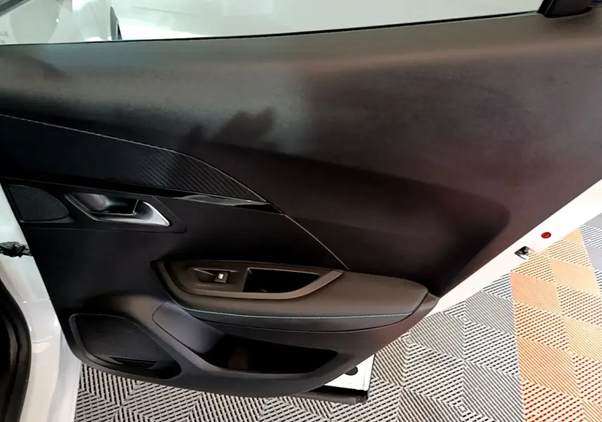 Vue intérieure de la porte avant gauche du Peugeot 2008 blanc, avec garniture noire et poignée argentée.