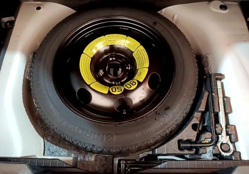 Vue plongeante sur la roue de secours noire avec étiquette jaune et outils de bord dans le coffre d’un Peugeot 2008 blanc.