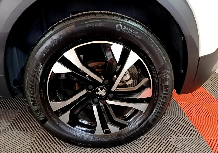 Gros plan sur la roue avant droite d’un Peugeot 2008 blanc, jante alliage noire et argent avec logo lion central.