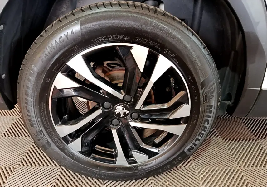 Gros plan sur la roue avant gauche d’un Peugeot 2008 blanc, avec jante alliage noire et argentée au design moderne.