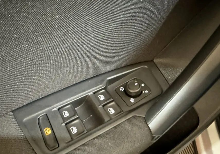 Vue rapprochée des commandes de lève-vitres et rétroviseurs sur la porte côté conducteur d’un Volkswagen Tiguan gris clair.