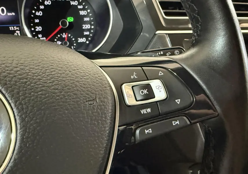 Gros plan sur le volant cuir noir du Volkswagen Tiguan 2020, avec commandes multifonctions et tableau de bord en arrière-plan.