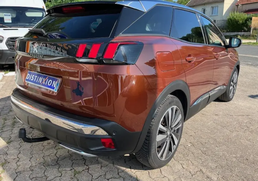 Vue 3/4 arrière droite d'un Peugeot 3008 2016 métallisé cuivre avec attelage démontable et feux arrière à griffes rouges.